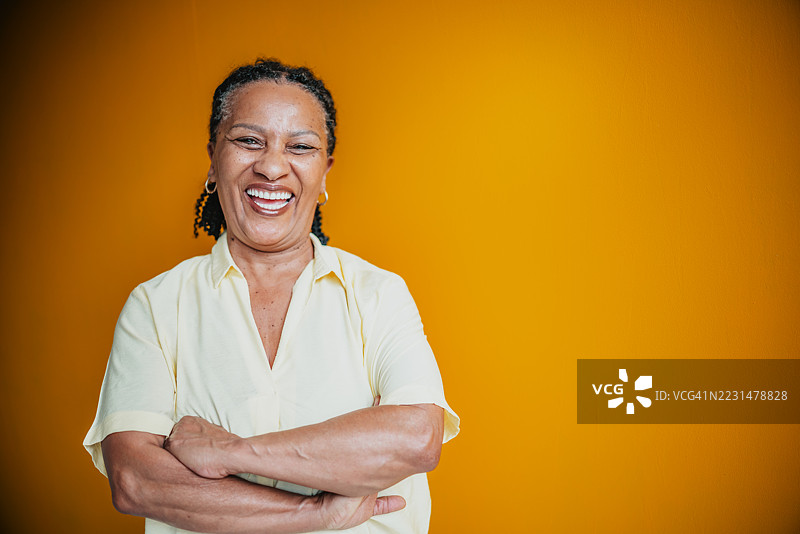 一位微笑的老年女性在充满活力的黄色背景下，展现出快乐和自信的气息。图片素材
