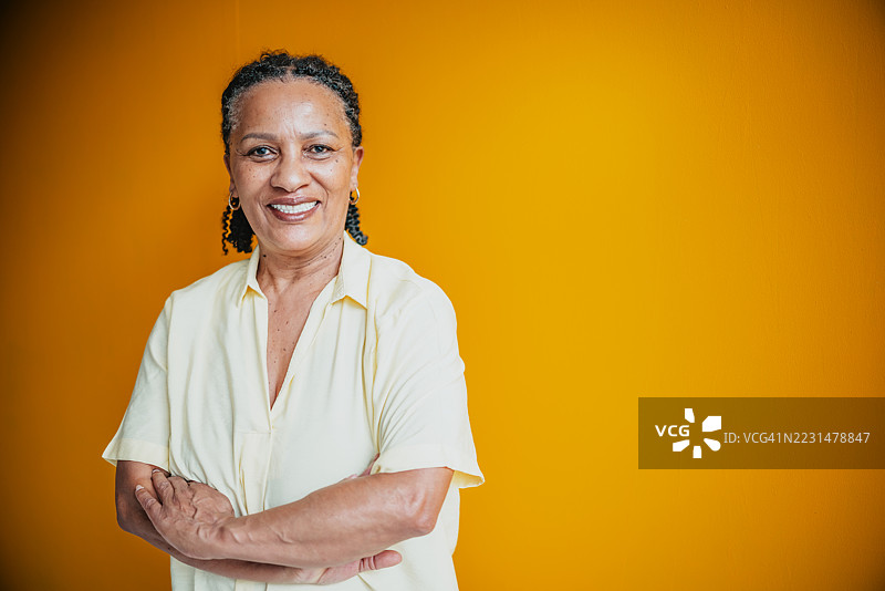 一位自信微笑的老年女性，背景为鲜艳的黄色，展现退休生活的快乐。图片素材