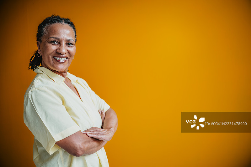 一位自信微笑的老年女性，背景为生动的黄色，置身于室内摄影棚环境中图片素材