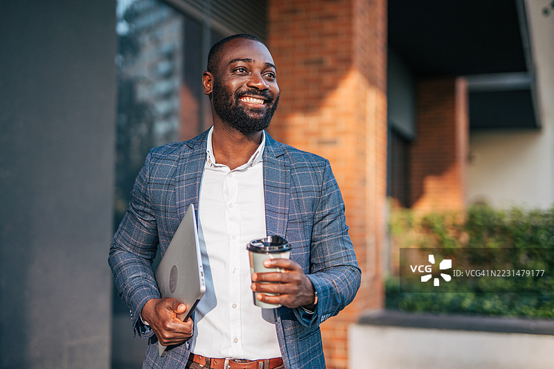 微笑的商人手拿笔记本电脑和咖啡走路图片素材
