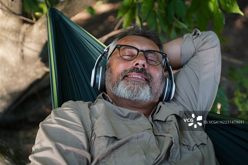 老年人在大自然中放松地躺在吊床上听音乐图片素材
