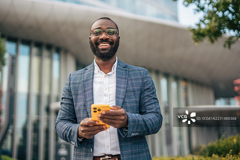 微笑的商人在城市环境中使用智能手机图片素材