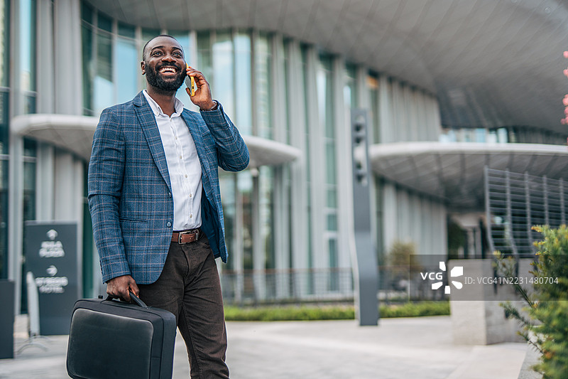 微笑的商人在办公室外走动并打电话图片素材