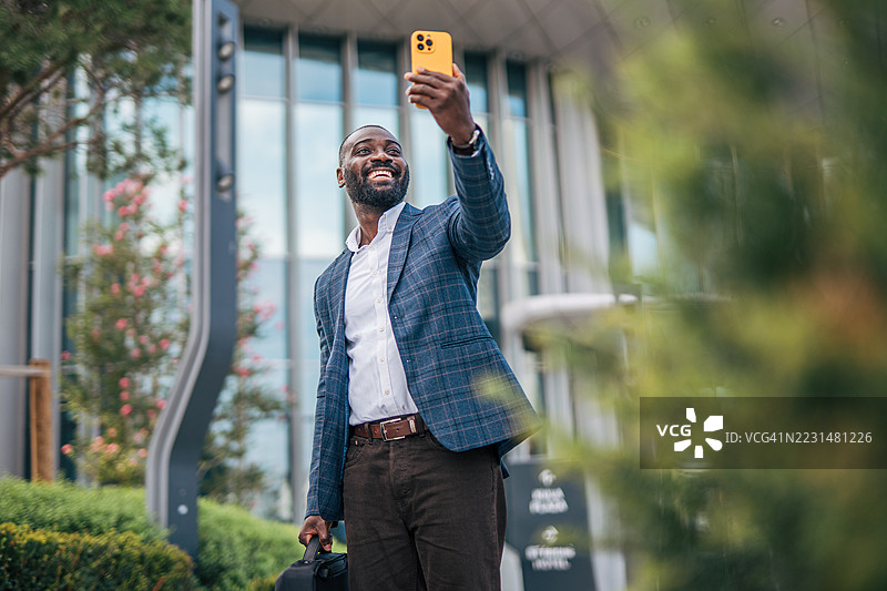 微笑的商人在办公大楼外自拍图片素材