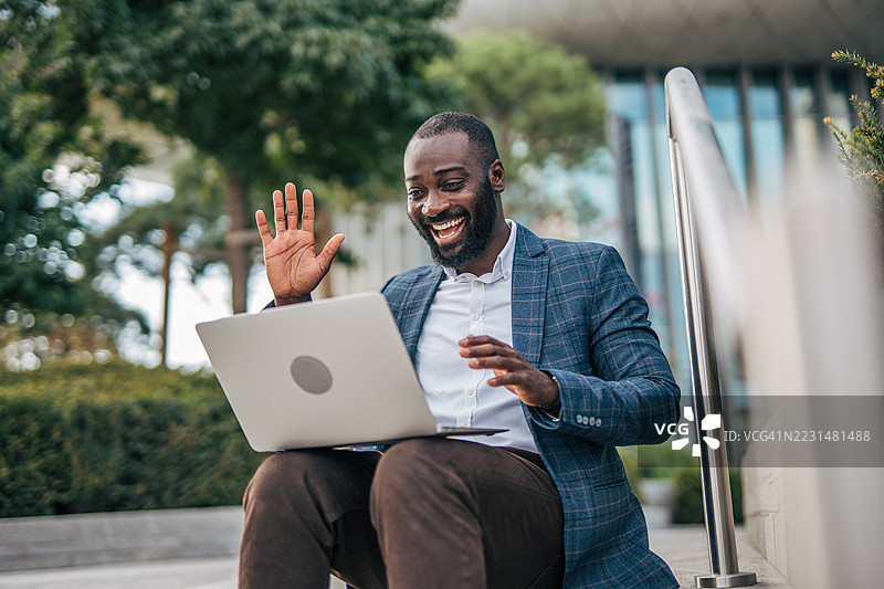 商人在户外通过笔记本电脑进行视频通话时挥手致意图片素材
