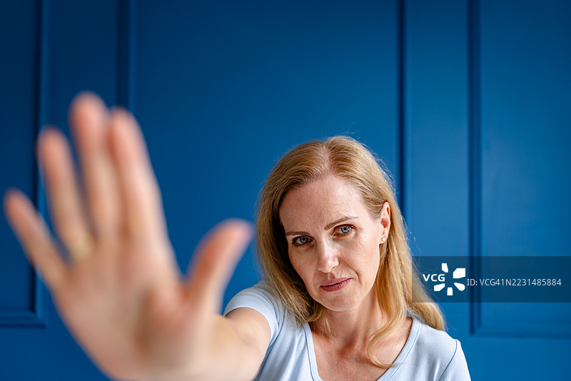 自信的女性在鲜艳的蓝色背景前摆姿势，手举起。图片素材