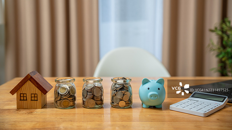 房屋模型。木桌上有储蓄罐和装满硬币的玻璃罐。房地产投资。物业投资和抵押贷款财务。储蓄。预算和房贷。拥有权。图片素材