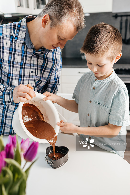 父亲和儿子在家里的厨房里烘焙心形巧克力蛋糕，将面糊倒入烤盘。图片素材