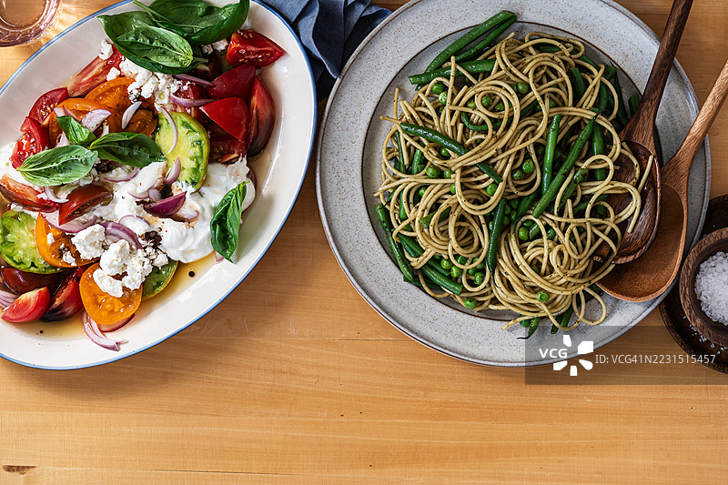健康的夏季餐点，沙拉配番茄、奶酪、酸奶，以及新鲜的青豆和豌豆的香蒜意面图片素材