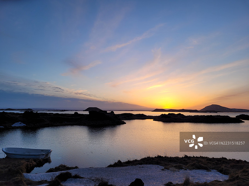 宁静的日落映照在平静的海面上，远处有岛屿。图片素材