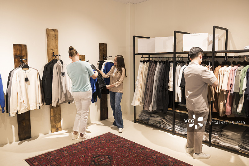 年轻女性在现代服装店里与店员一起挑选衣服图片素材