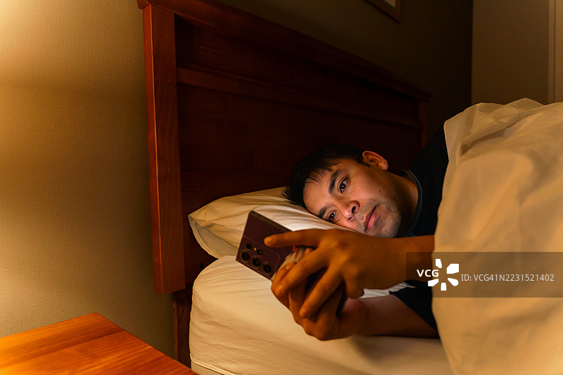 拉丁美洲男子在床上夜间使用智能手机图片素材