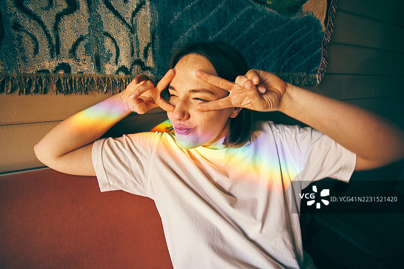 五彩斑斓的彩虹光线照在摆出和平手势的女人身上图片素材