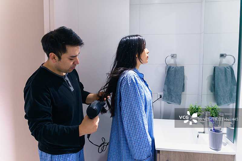 拉丁美洲男子在浴室为女子吹干头发图片素材