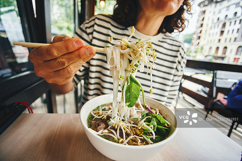 在咖啡馆里吃新鲜面条汤，配有绿叶蔬菜和豆芽的人图片素材
