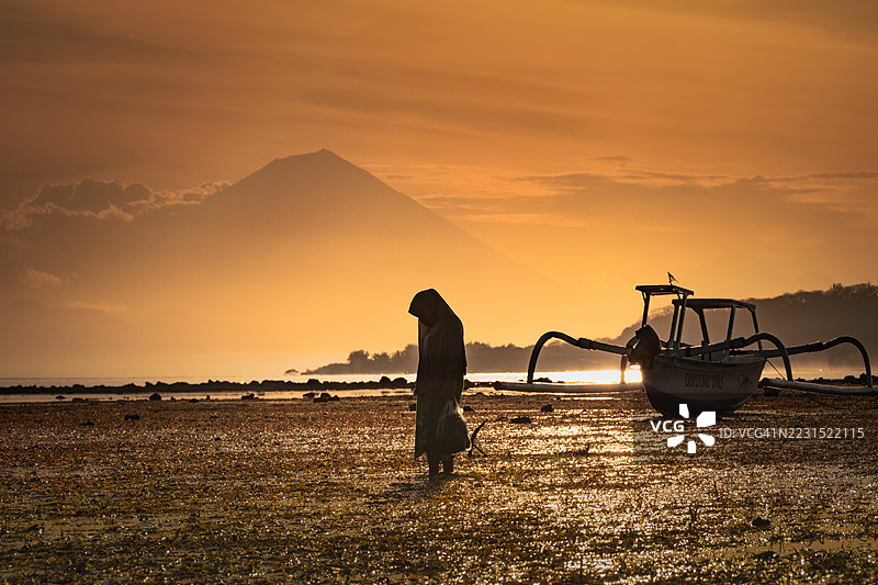 日落时分，海滩上走着的女性剪影，背景中有一艘船，吉利艾尔，印度尼西亚图片素材
