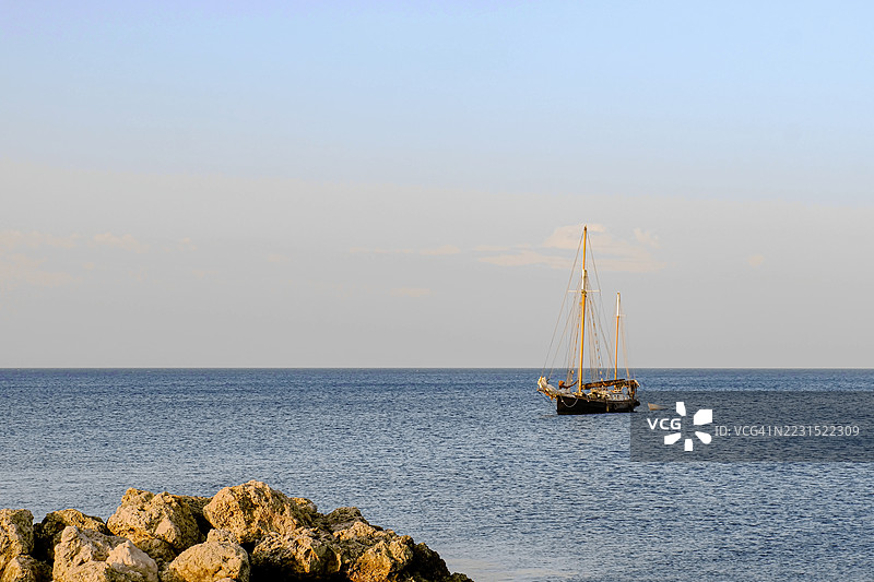 平静海面上的帆船与岩石海岸图片素材