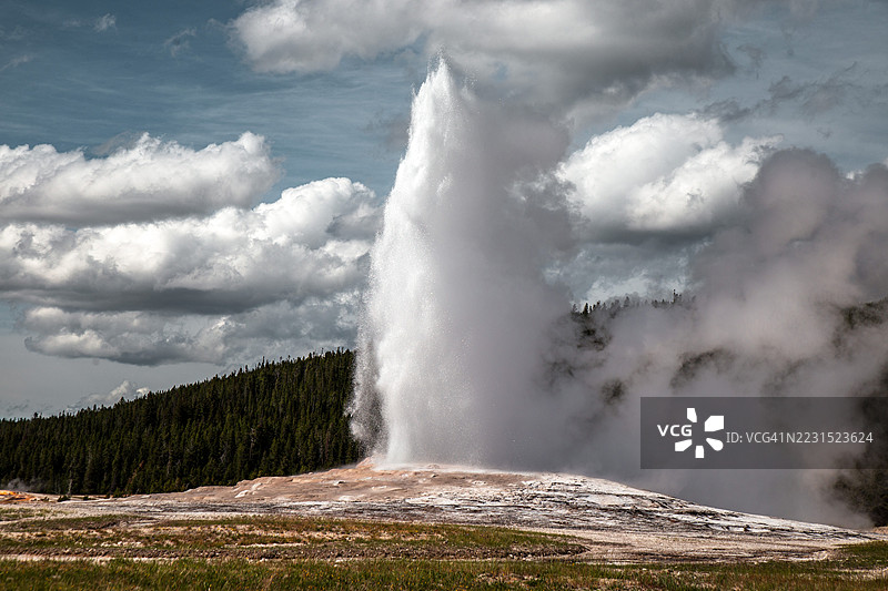 在多云的天空下，老忠实间歇泉壮观的喷发，位于美国图片素材
