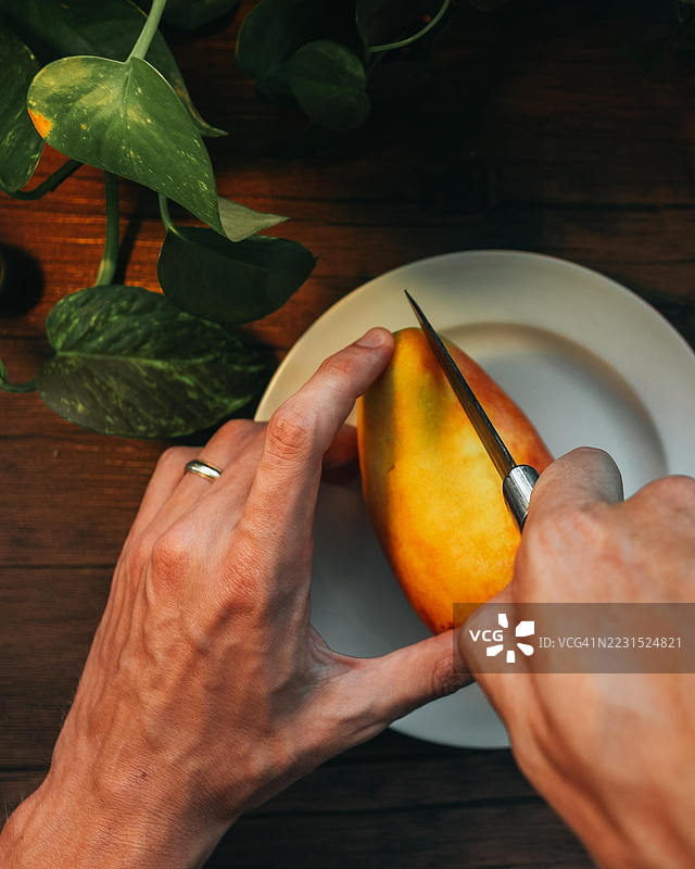 手在木桌上切割芒果，旁边有绿色的叶子图片素材