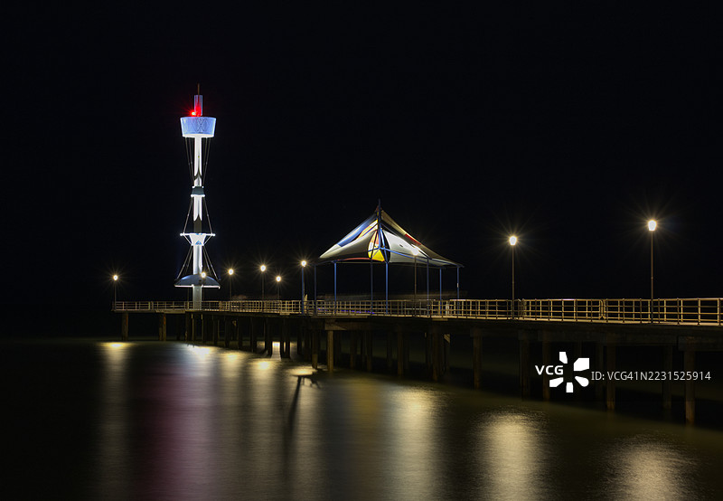 夜晚布莱顿，澳大利亚，灯光照亮的码头和灯塔在水面上倒影图片素材
