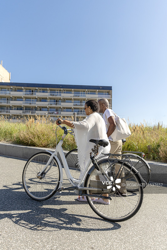 多元化的老年夫妇在荷兰海滩享受阳光明媚的夏日骑行时光图片素材