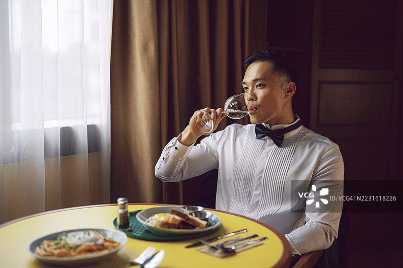 年轻亚洲男子穿着正式服装在餐桌上喝酒图片素材