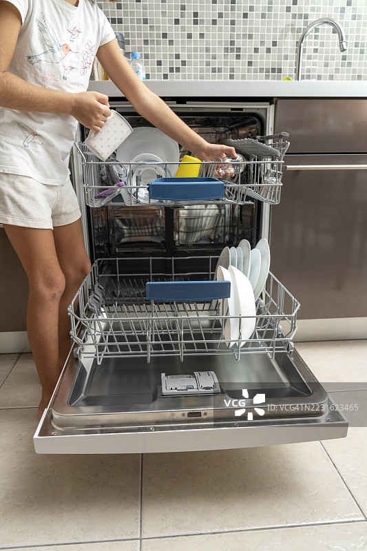 厨房里打开的洗碗机，里面是干净的碗碟。小女孩在现代厨房里卸洗碗机。图片素材