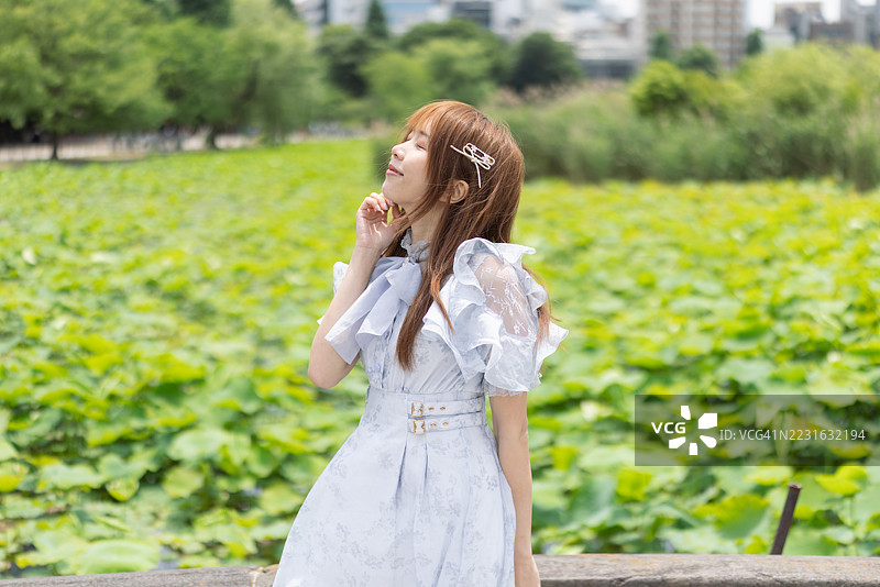 年轻女性游客穿着浅蓝色连衣裙，在公园里深呼吸图片素材