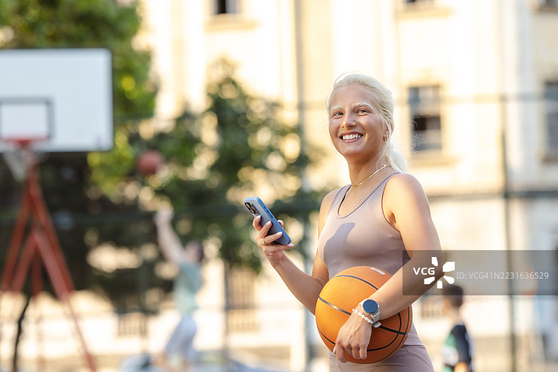 活跃的女性在户外打篮球时查看她的智能手机图片素材