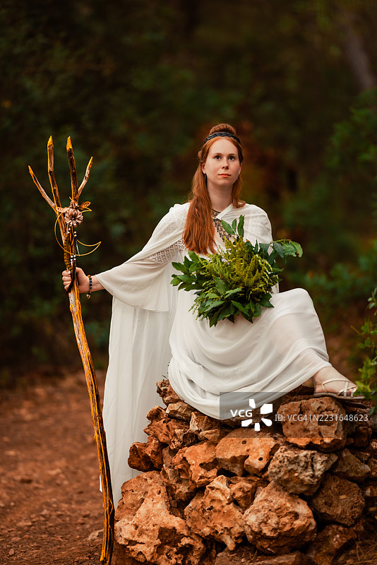 坐在魔法森林石丘上的凯尔特女萨满，手持法杖和草药。图片素材