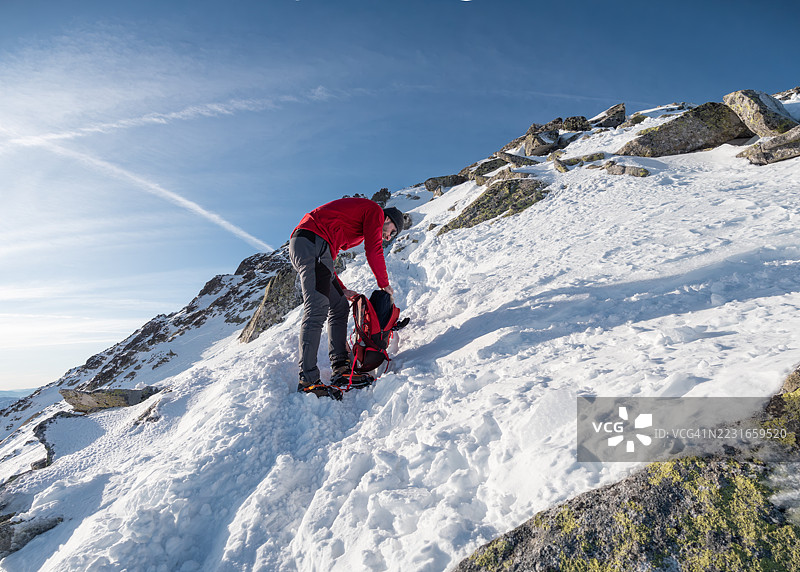 一名登山者在雪山中重新整理他的背包。图片素材