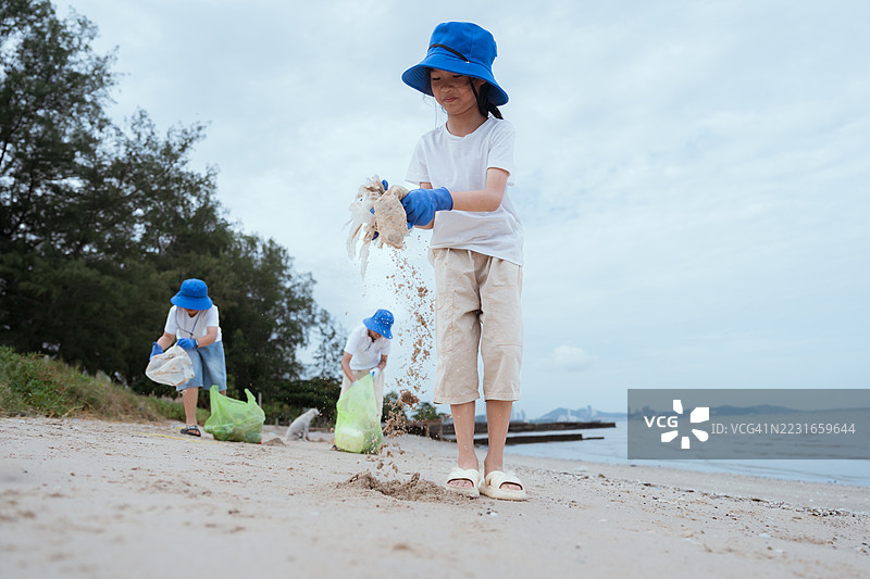 孩子们在夏天的阴天里，戴着蓝色帽子和手套清理海滩。图片素材