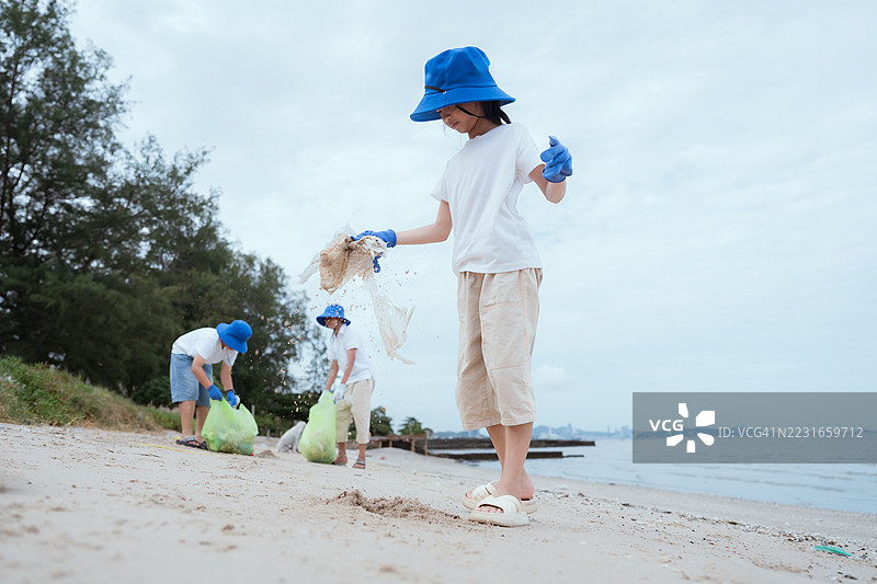 孩子们在夏天的阴天里戴着蓝色帽子和手套清理海滩图片素材