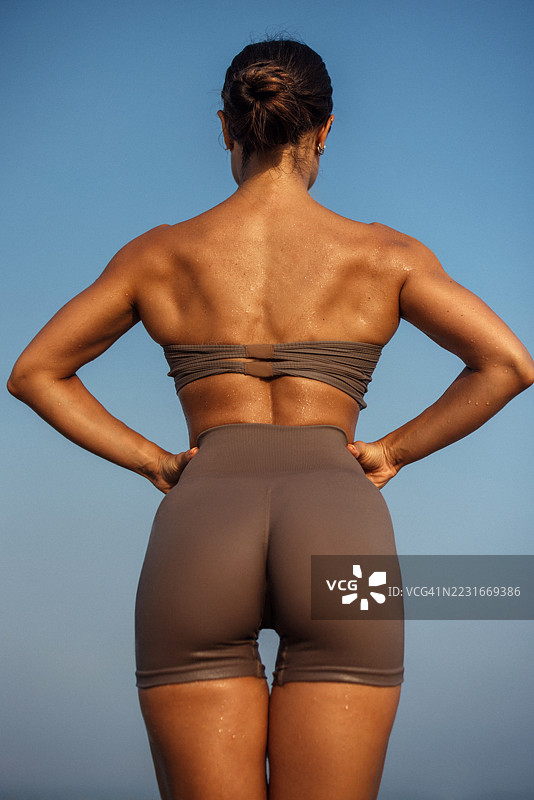 穿着运动服的健美女性在晴朗的天空下，背影展示了结实的背部。图片素材