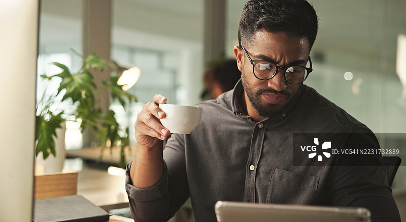 专业男士在办公室里一边享用咖啡一边使用平板电脑工作图片素材