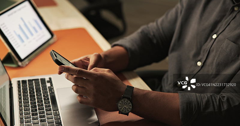 在工作站使用智能手机的人，旁边有笔记本电脑和图表视图图片素材
