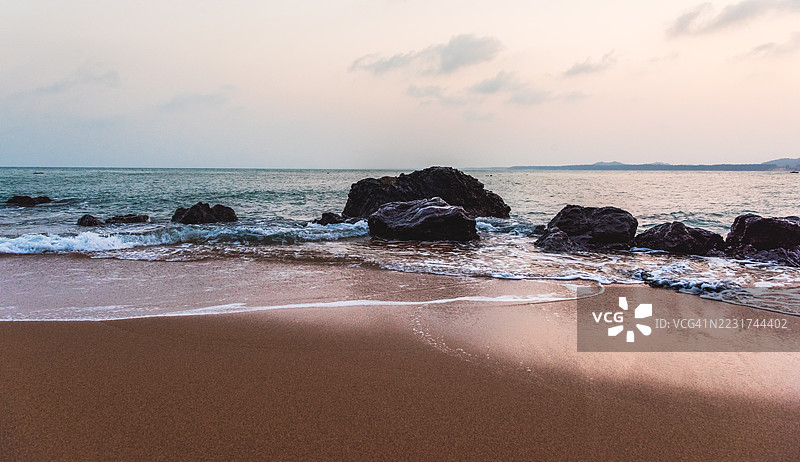 黄昏时分宁静的海滩场景，波浪与岩石相伴图片素材