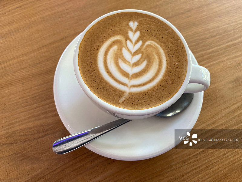 白色咖啡杯中的扁平白咖啡，上面有蕨类图案的拿铁艺术，放在咖啡桌上。图片素材