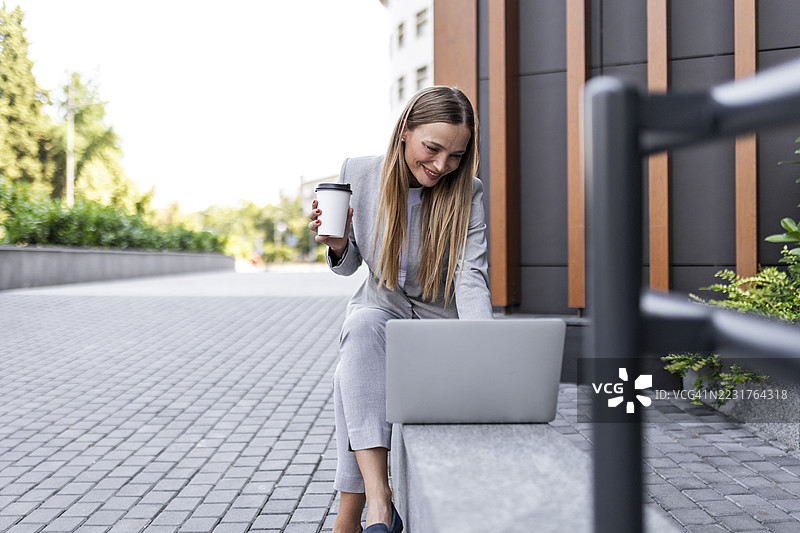 时尚的职业女性在办公室附近一边享受咖啡一边使用笔记本电脑图片素材