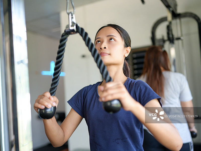 年轻女性在健身房使用带绳附件的拉索机锻炼，专注于她的训练。环境明亮现代，倡导健康的生活方式和健身。图片素材