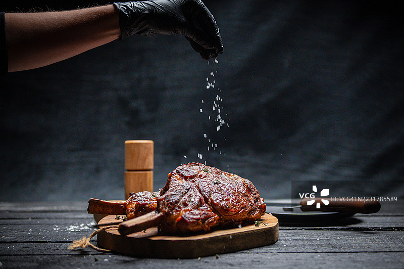 厨师在粗犷的砧板上给烤牛排撒盐图片素材
