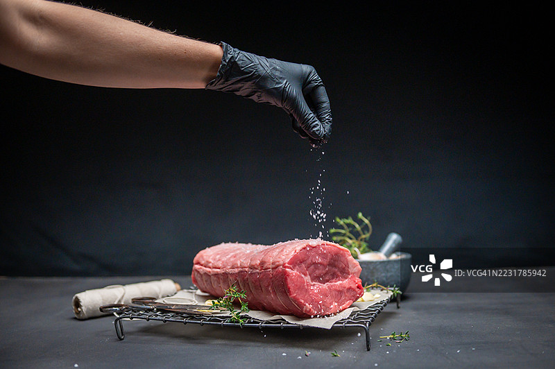 厨师在昏暗的环境中向生牛肉切块撒盐图片素材