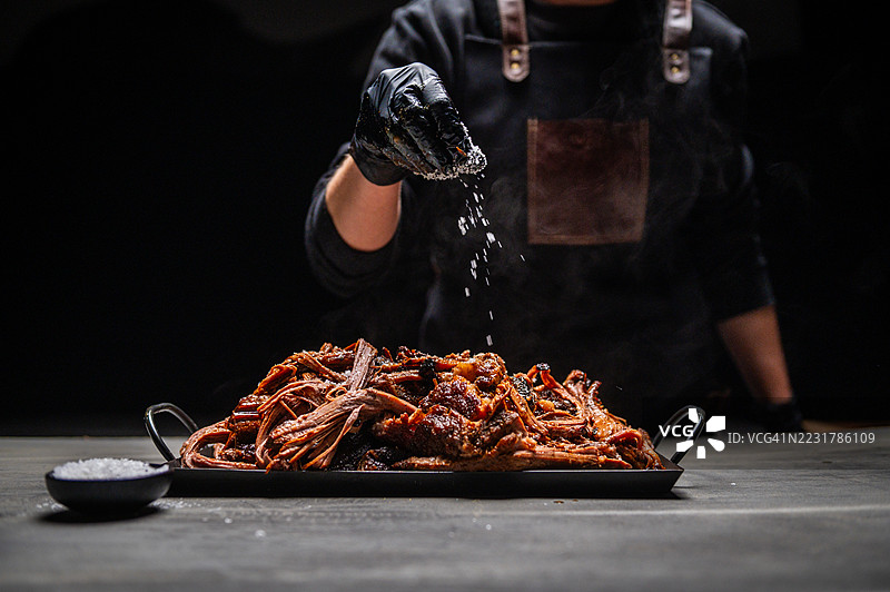 厨师在戏剧性的灯光下给烧烤肉添加盐图片素材