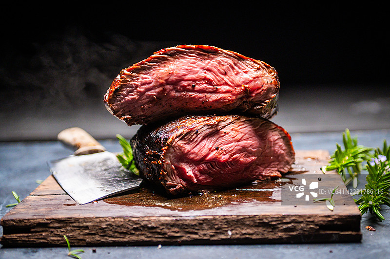 多汁的切片牛排放在粗犷的木板上，旁边有一把刀图片素材