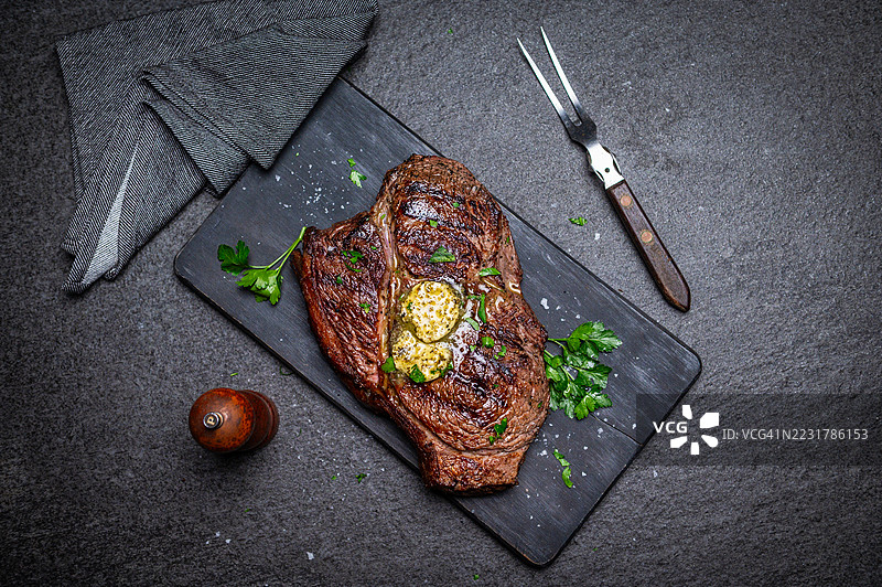 多汁的烤牛排，配有黄油和新鲜香菜，摆放在石板上图片素材