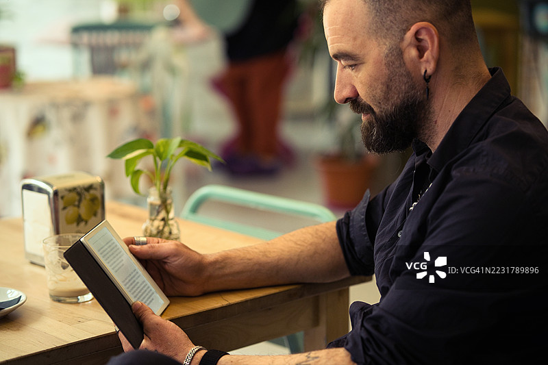 现代成年人在悠闲的咖啡馆里阅读电子书，留着莫霍克发型。图片素材