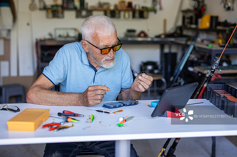 老渔夫在平板电脑上观看设置钓鱼装备的说明图片素材