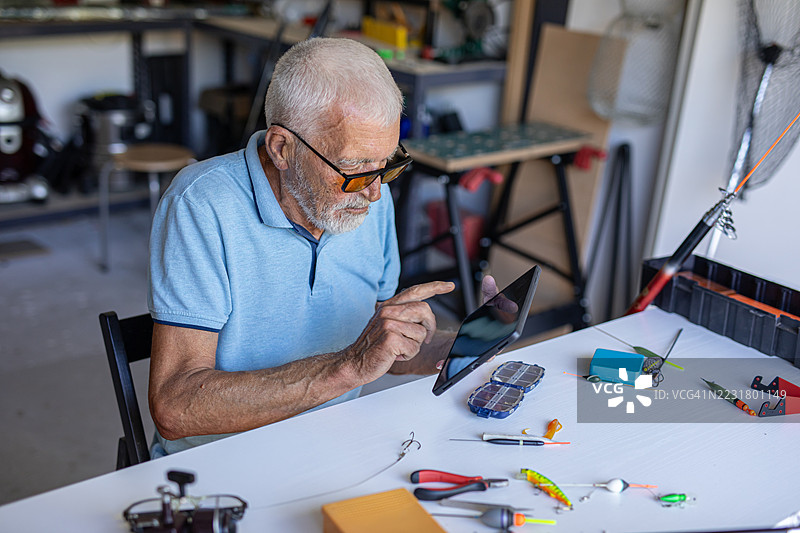 退休老人一边准备钓鱼装备，一边在平板电脑上观看教程图片素材