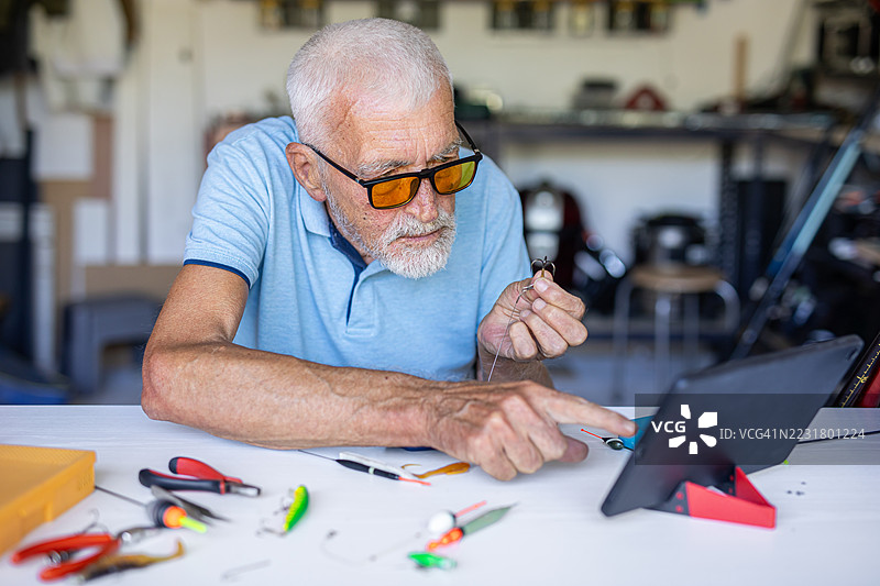 退休老人一边准备钓鱼装备，一边在平板上观看教程图片素材