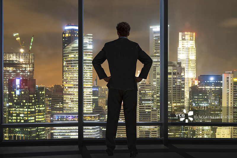 商人在办公室窗前俯瞰现代城市。图片素材